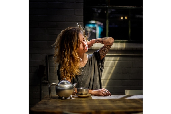 Girl rubs neck at table with tea or coffee.
